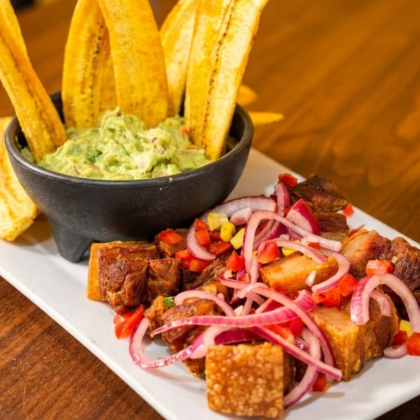 Crispy pork belly with red onion, bell peppers, and a side of guacamole with plantain chips.